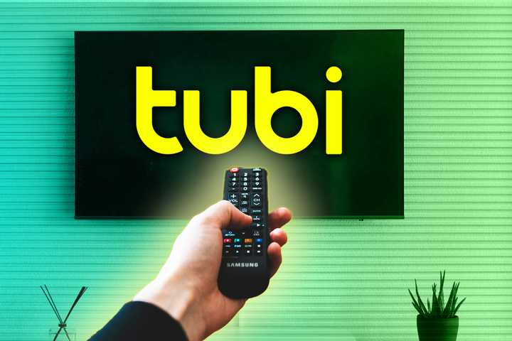 A person pointing a remote at a TV with the Tubi logo on it. 