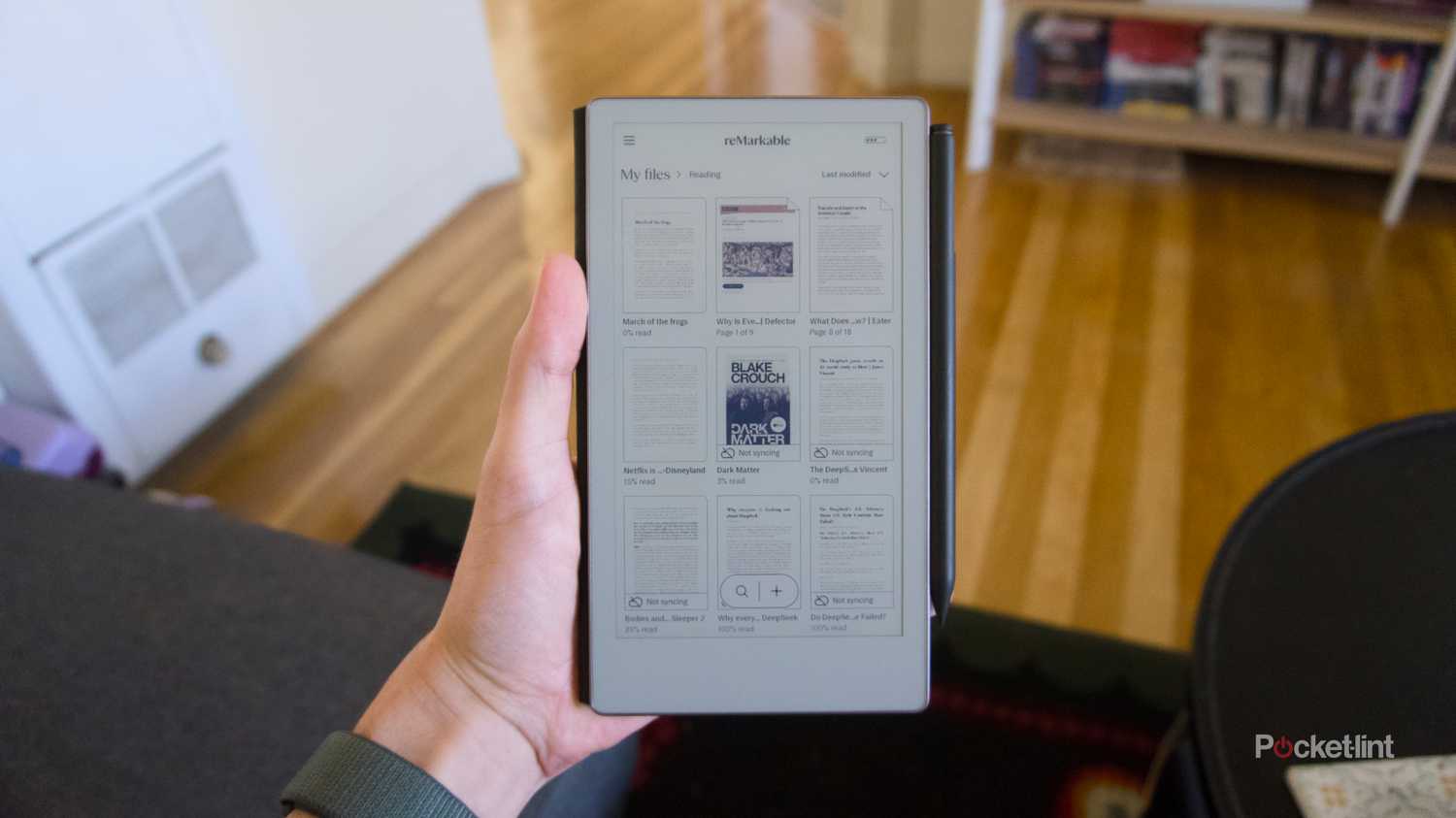 A hand holding a reMarkable Paper Pro Move displaying a page full of imported articles.