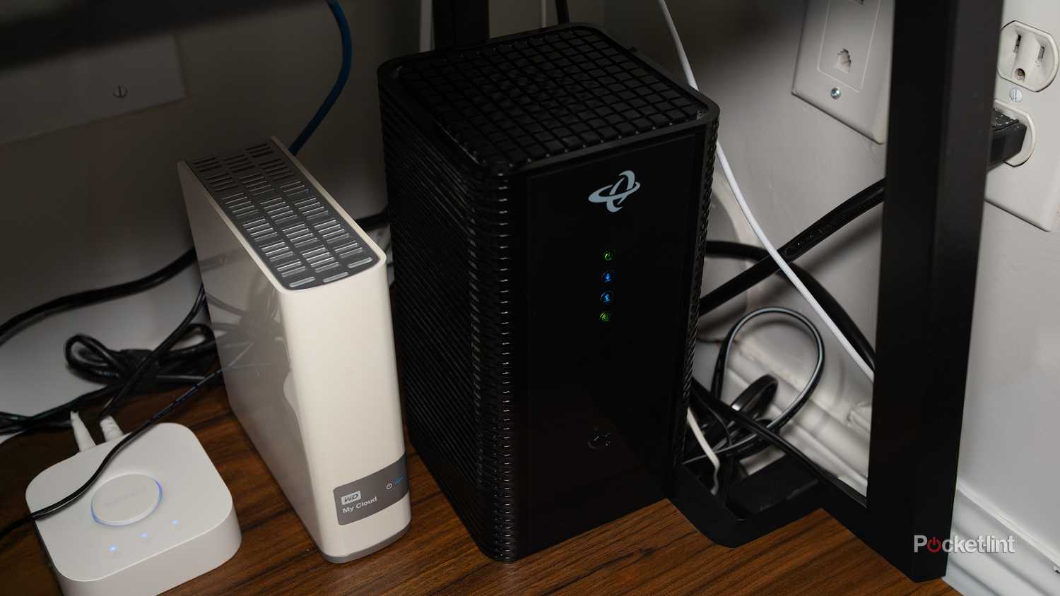 A Wi-Fi router sitting on a shelf next to a backup drive and a Philips Hue Bridge.